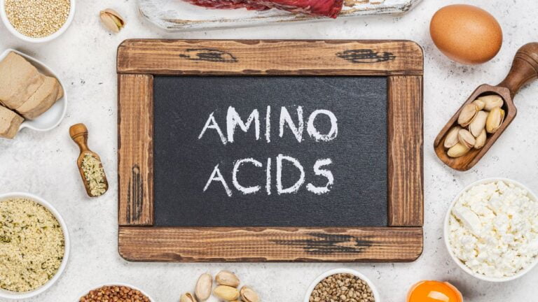 Tabla de pizarra con la inscripción 'AMINO ACIDS' y una selección de alimentos proteicos, ilustrando una lista de fuentes de los 10 aminoácidos no esenciales