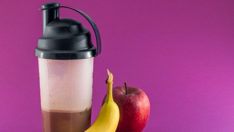 Batido de proteínas junto a frutas y pesas, ejemplificando una preparación común para el pre entreno en el régimen de un atleta.