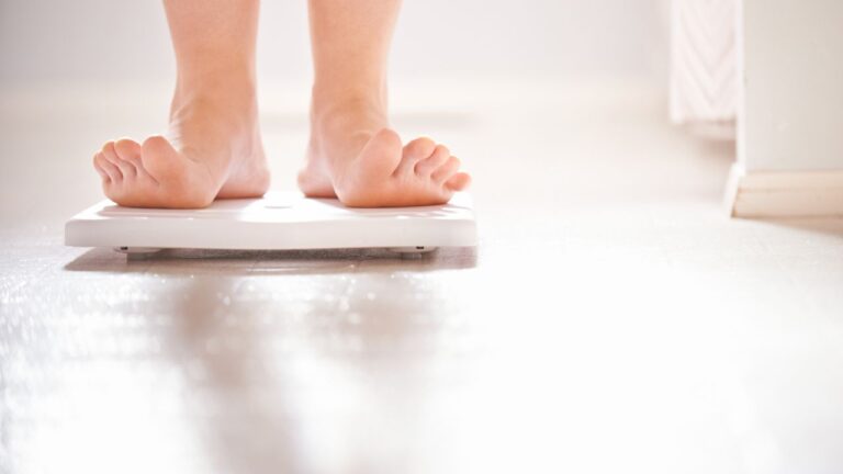 Pies descalzos sobre una báscula en un baño, indicando el acto de pesarse como parte de la rutina de control de peso