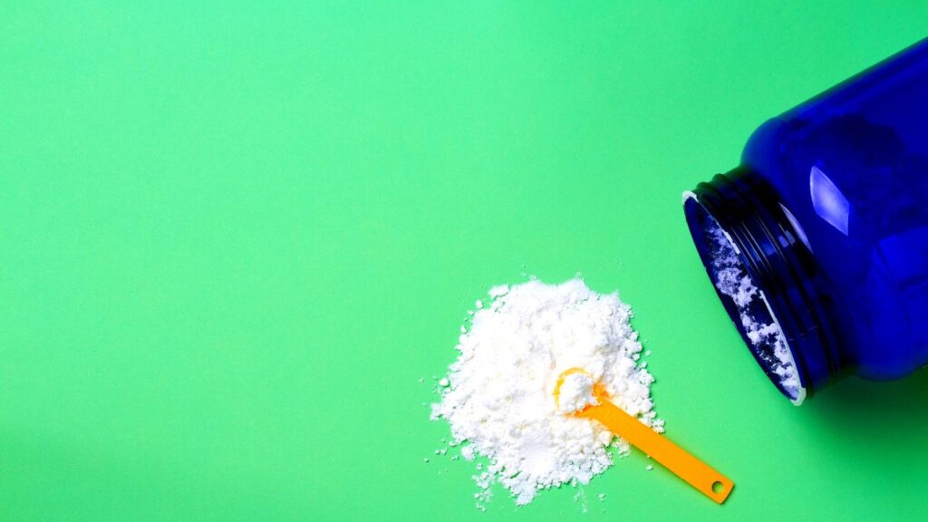 Suplemento de creatina monohidratada derramado de una cuchara amarilla, destacando la forma cruda de los suplementos de entrenamiento.