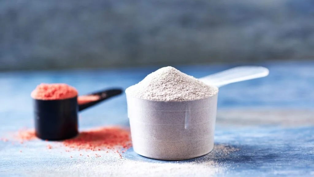 Cucharas con diferentes tipos de proteína en polvo y creatina sobre superficie de madera, relacionado con el aumento de masa muscular