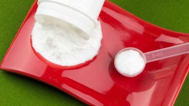 Suplemento de creatina en polvo con cuchara dosificadora sobre fondo rojo, enfocado en los beneficios para el entrenamiento