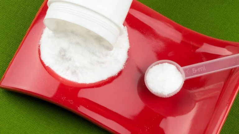 Suplemento de creatina en polvo con cuchara dosificadora sobre fondo rojo, enfocado en los beneficios para el entrenamiento