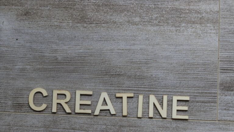 Letras de madera formando la palabra creatina sobre fondo de madera, conceptualizando suplementos deportivos.
