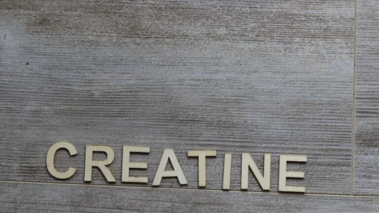 Letras de madera formando la palabra creatina sobre fondo de madera, conceptualizando suplementos deportivos.