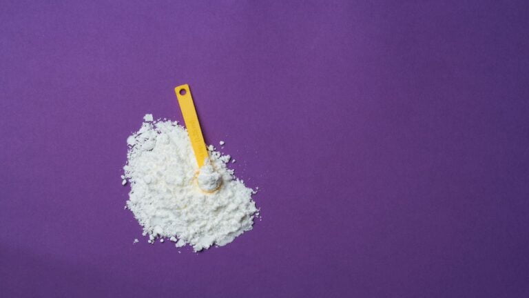 Montón de creatina en polvo con cuchara medidora amarilla sobre fondo morado, destacando la suplementación deportiva.