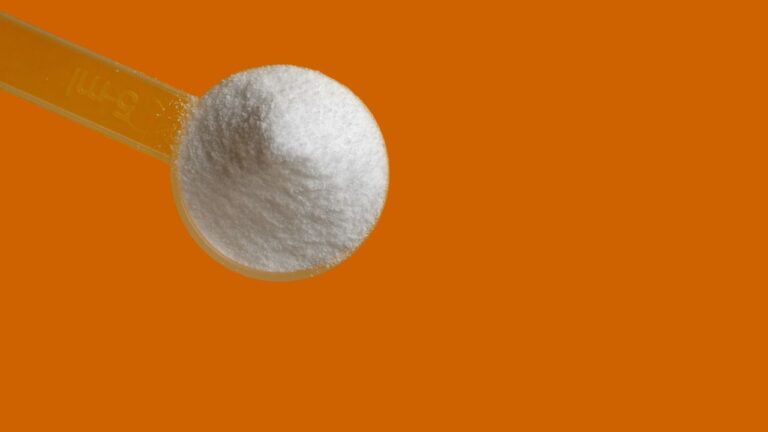 Cucharada de suplemento de creatina pura sobre fondo naranja, enfoque en la dosificación para la optimización del rendimiento.