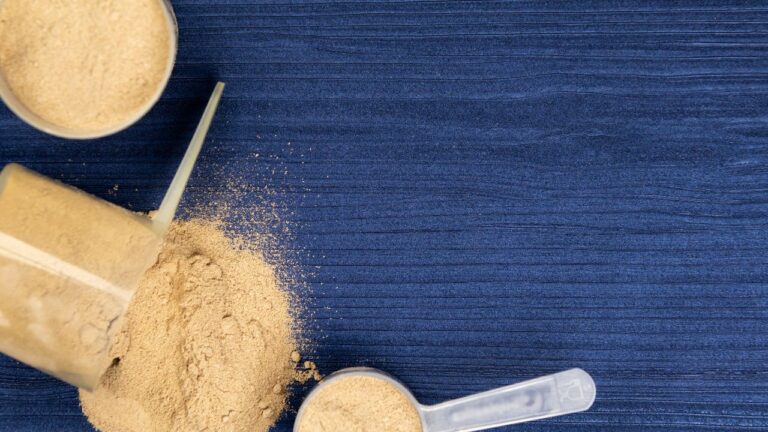 Polvo de suplemento proteico disperso, ideal para antes o después de entrenar, sobre mesa azul.