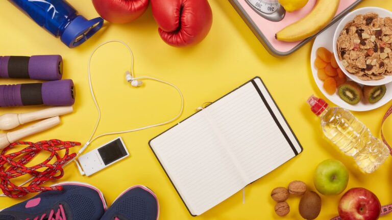 Equipo de fitness y nutrición con mancuernas, cuaderno y alimentos integrales, enfocados en el seguimiento de la condición física y la dieta.
