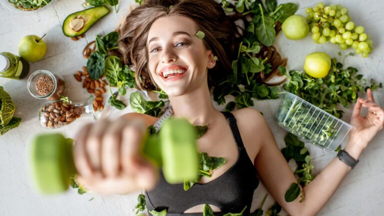 Sonriente mujer haciendo ejercicio con mancuernas verdes, rodeada de alimentos nutritivos, enfatizando la alegría en un estilo de vida activo y saludable.