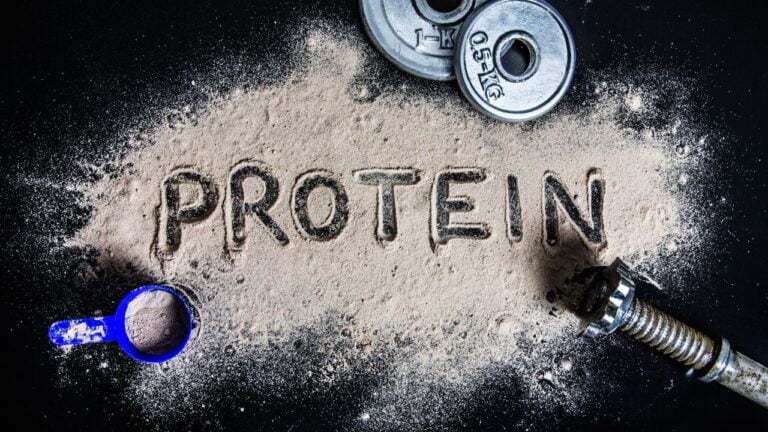 Inscripción de 'PROTEIN' hecha con polvo de proteína y material de gimnasio, representando la integración del suplemento en el entrenamiento.