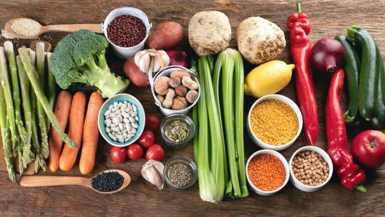 Variedad de verduras y legumbres frescas, fuentes de antioxidantes naturales, sobre una mesa de madera.