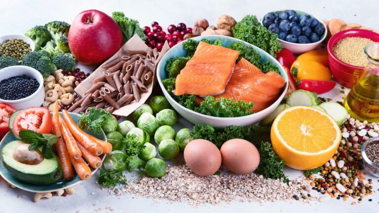 Bol con salmón y vegetales verdes junto a frutas y cereales integrales, ricos en nutrientes beneficiosos para la salud.