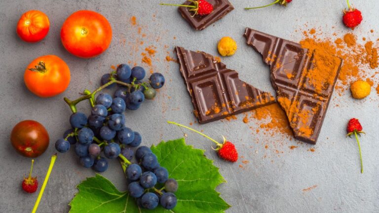 Trozos de chocolate oscuro con polvo de cacao, rodeado de frutas y bayas que contienen antioxidantes.