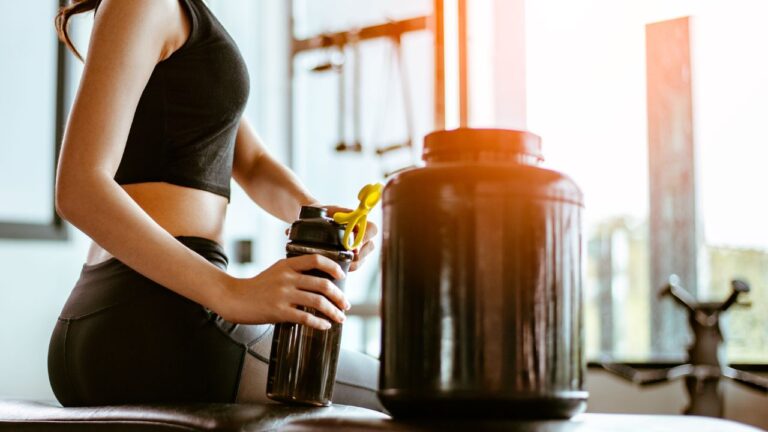Atleta preparando un batido de suplementos junto a un bote grande de creatina micronizada.