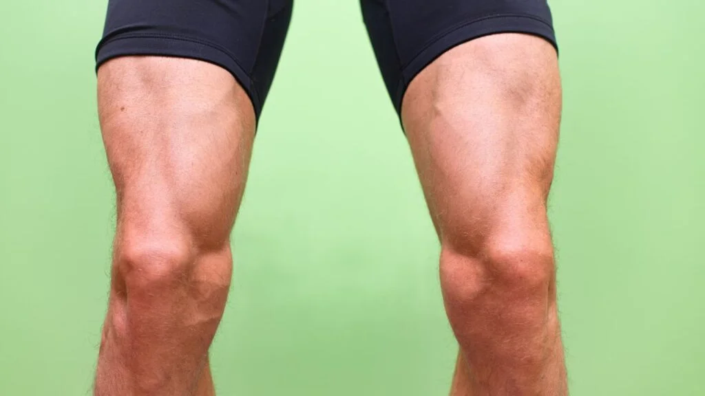 Primer plano de piernas musculosas, enfocando en los cuádriceps, sobre fondo verde para destacar la musculatura desarrollada en entrenamientos caseros.