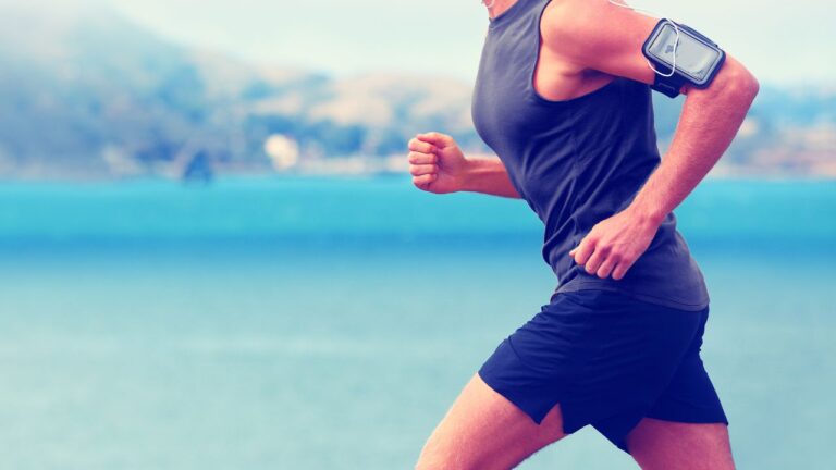 Corredor con brazalete para smartphone manteniendo su ritmo de carrera cerca del agua, demostrando una forma efectiva de cardio para la pérdida de peso.