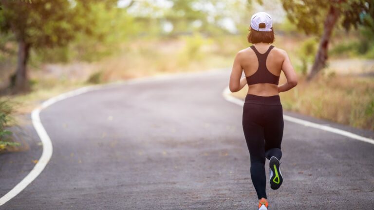 Atleta femenina corriendo por un camino solitario, integrando el running en su rutina de entrenamiento.