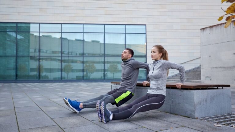 Pareja realizando fondos en banco para ejercitar tríceps al aire libre.