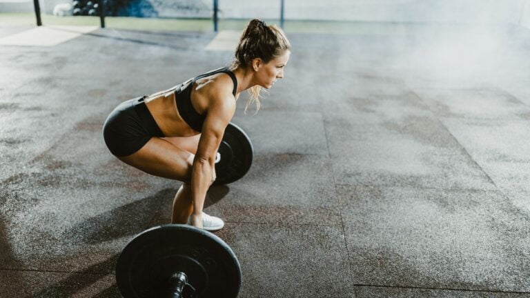 Entrenamiento individual de peso muerto con barra por una atleta enfocada, demostrando fuerza y técnica en el gimnasio.