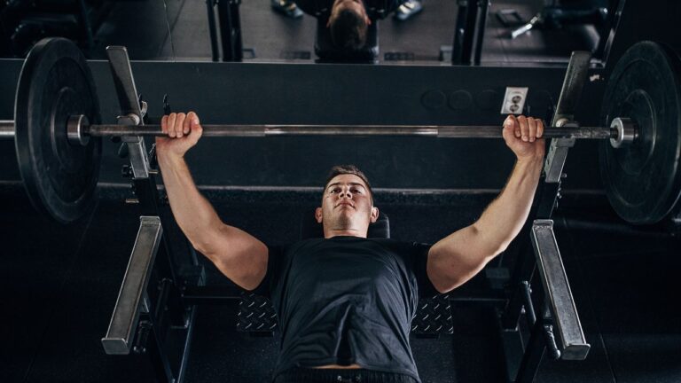 Hombre realizando un ejercicio de levantamiento de barra en banco plano en el gimnasio.