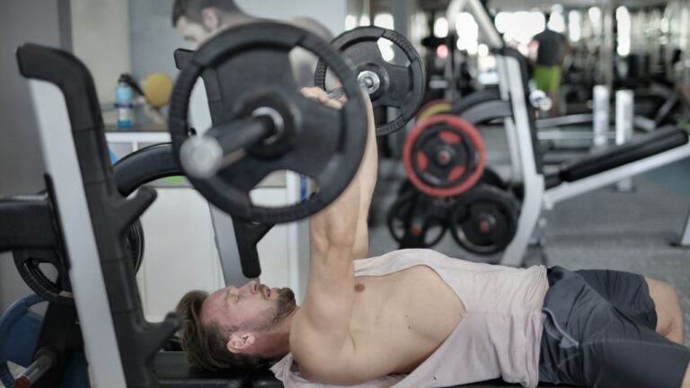 Levantamiento de barra en banco por un deportista enfocado en el gimnasio.