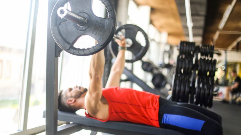 Hombre entrenando pectorales con press en banco declinado en una sala de musculación iluminada.