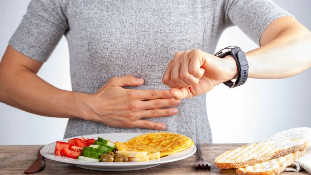 Persona mirando la hora en su reloj deportivo mientras tiene un plato de comida delante, reflejando la planificación en el ayuno intermitente.