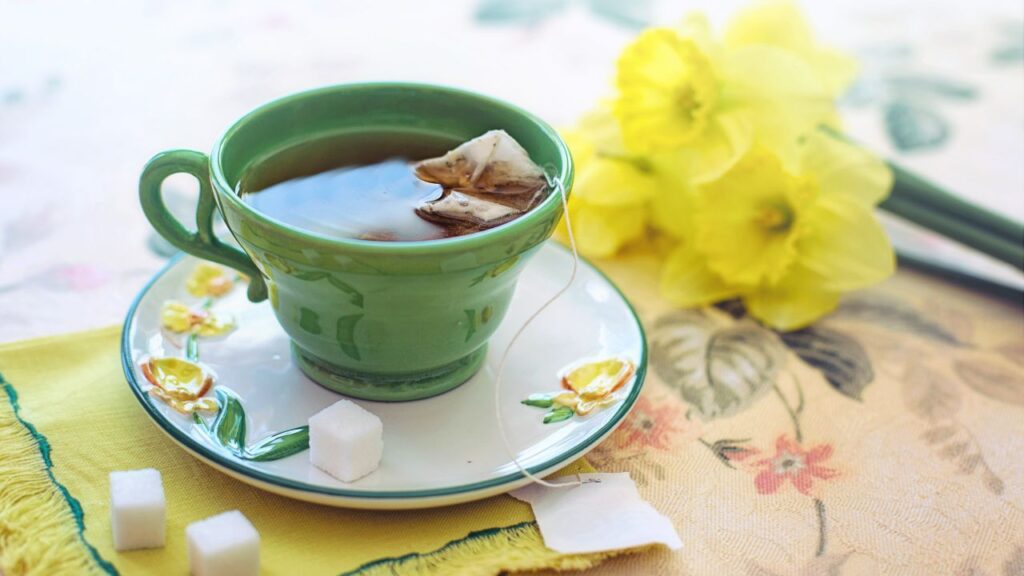 Taza de té verde con bolsita de infusión acompañada de flores amarillas primaverales