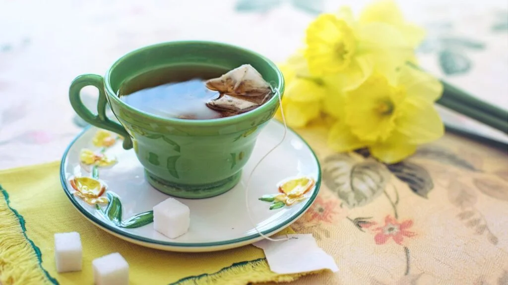 Taza de té verde con bolsita de infusión acompañada de flores amarillas primaverales