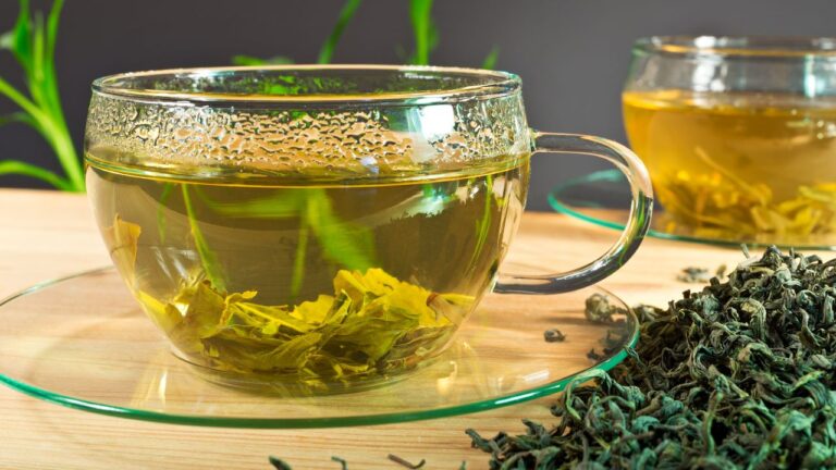 Infusión transparente en taza de vidrio con hojas de té verde sueltas en primer plano