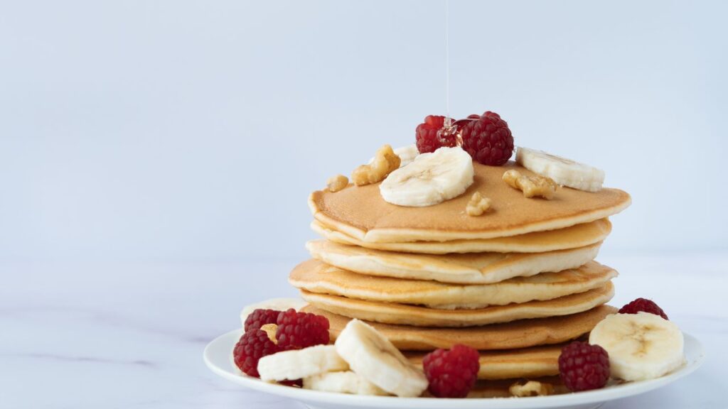 Pancakes esponjosos con plátano y frambuesas, un desayuno energizante para atletas y deportistas.