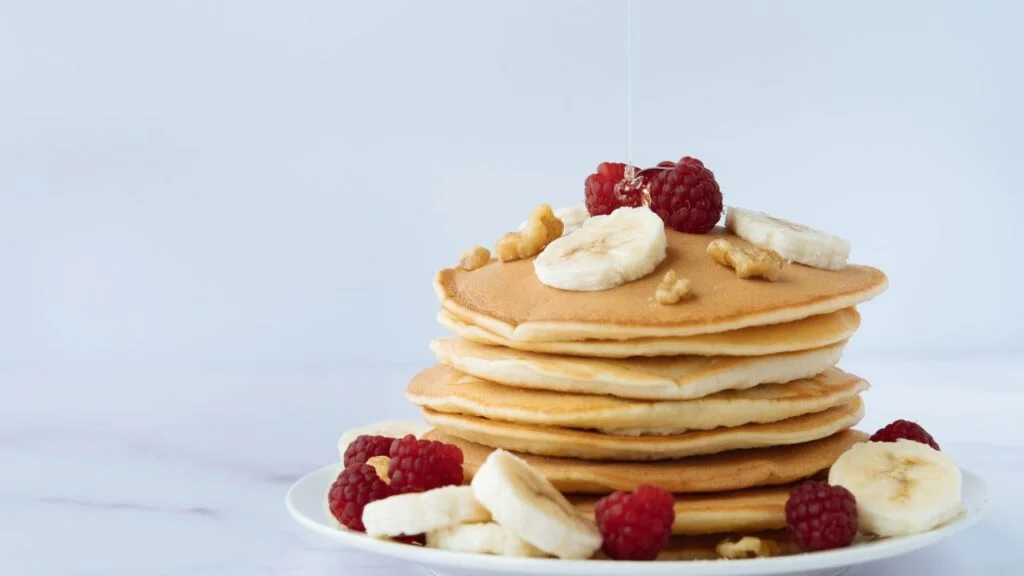 Pancakes esponjosos con plátano y frambuesas, un desayuno energizante para atletas y deportistas.
