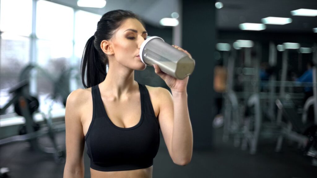 Una atleta bebiendo un batido de proteína posentrenamiento, una elección popular para la recuperación muscular.