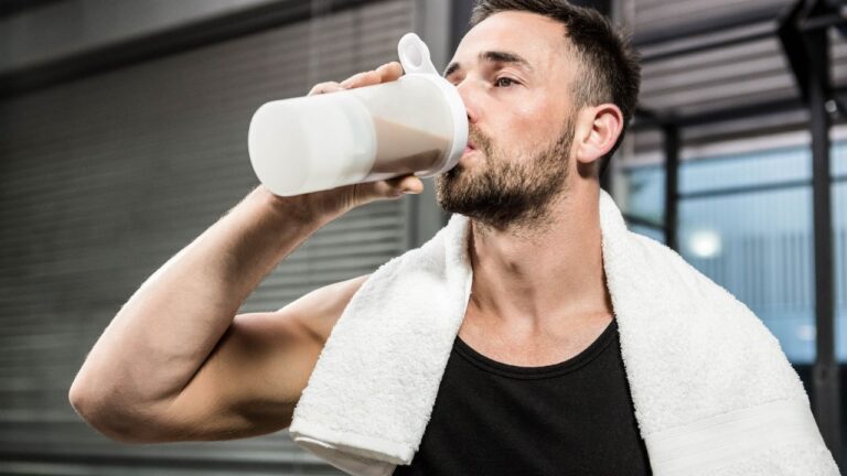 Atleta en el gimnasio tomando un descanso para rehidratarse con un batido rico en proteínas.