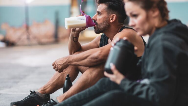 Dos deportistas sentados y descansando, uno de ellos consumiendo un batido nutritivo después de ejercitar.