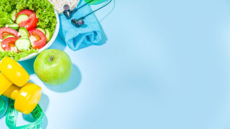 Manzana verde y pesas amarillas sobre fondo azul con toalla y auriculares, elementos para un estilo de vida activo y saludable