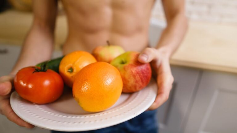 Plato con frutas y verduras sostenido por una persona con abdomen definido, representando los resultados de una alimentación balanceada y ejercicio.