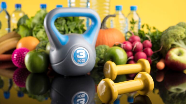 Pesas y alimentos nutritivos sobre fondo reflejante, fundamentales para una alimentación enfocada en la pérdida de grasa y el mantenimiento muscular.