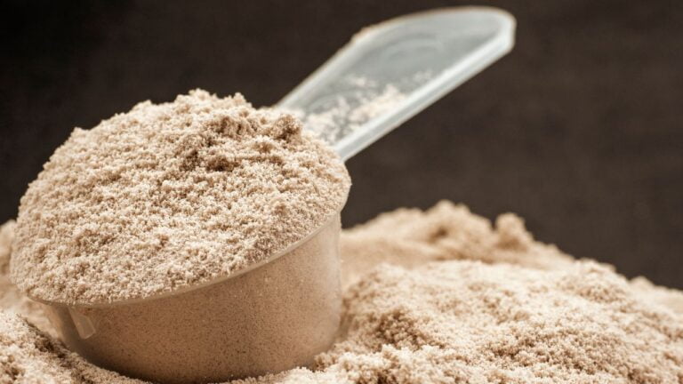 Cuchara con proteína en polvo sobre fondo neutro, suplemento popular para apoyar el desarrollo muscular y la recuperación.