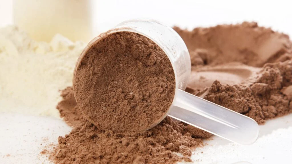 Proteína en polvo marrón en cuchara medidora con el fondo borroso, detalle de suplemento deportivo.