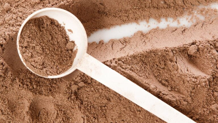 Cucharada de proteína en polvo de chocolate a punto de ser mezclada para un batido post-entreno.