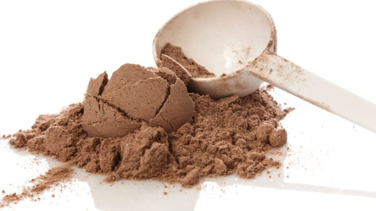 Polvo de proteína whey blanca en cucharón medidor sobre fondo claro, suplemento para dietas deportivas.