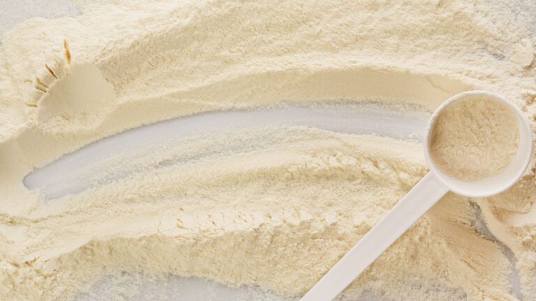 Montón de proteína de chocolate esparcida junto a una cuchara medidora, ingrediente para suplemento nutricional.
