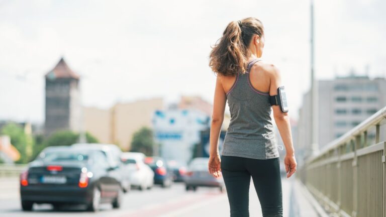 Mujer joven caminando por la ciudad con auriculares, un ejemplo de incorporar ejercicio en la rutina diaria para bienestar físico.