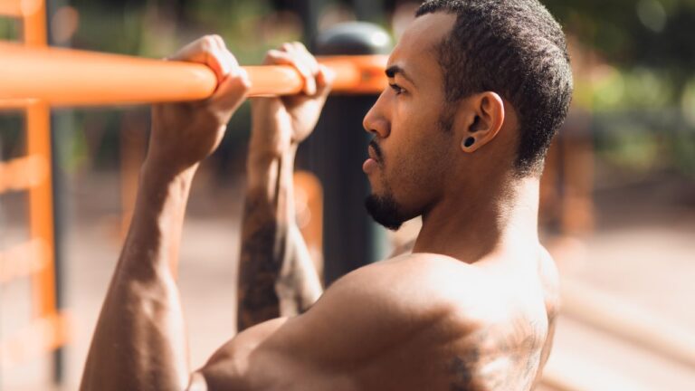 Un hombre concentra su fuerza mientras hace dominadas en una barra al aire libre, demostrando la intensidad de entrenamientos al estilo CrossFit que no requieren de material adicional.